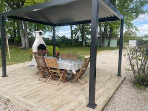 Eine überdachte Terrasse im Freien mit Tisch und Stühlen, einem Steinofen und einem Kiesboden.