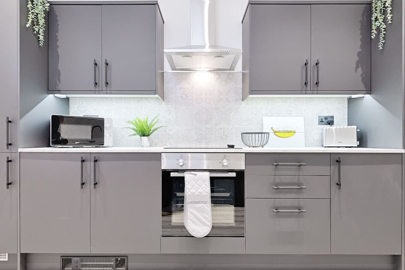 A modern kitchen with grey cabinets, a microwave, a toaster, and a hanging plant.