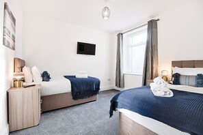 Ett hotellrum med två sängar, en TV, ett nattduksbord med en lampa och ett fönster med gardiner.
