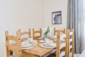 Ett matbord i trä, dukat med vita tallrikar och en vas med blommor.
