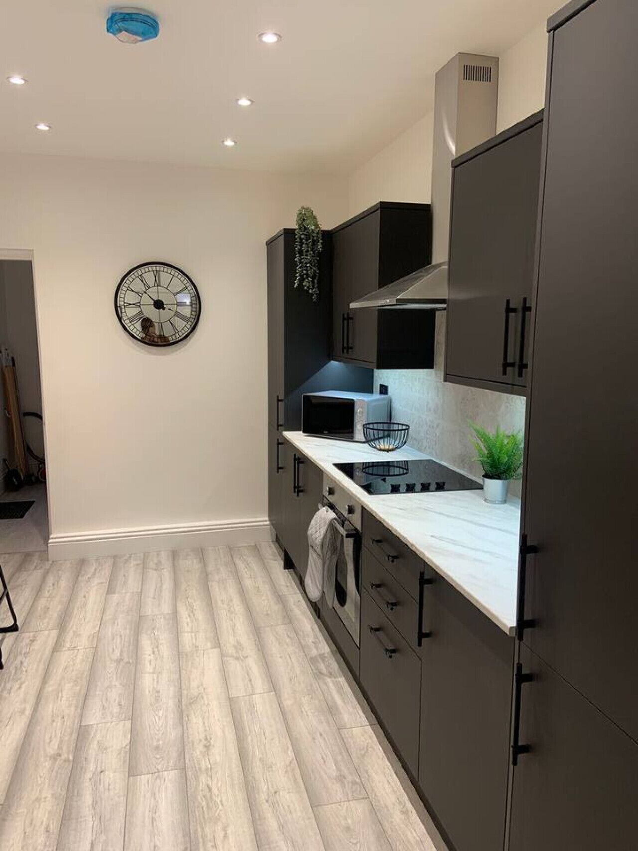 A modern kitchen with dark cabinets, a white countertop, a built-in microwave, and a wall clock.
