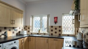 A kitchen with wooden cabinets, a washing machine, a sink, and two windows with a view. - 5 Bed Home • Parking • Ideal for Contractors (Carmarthenshire)