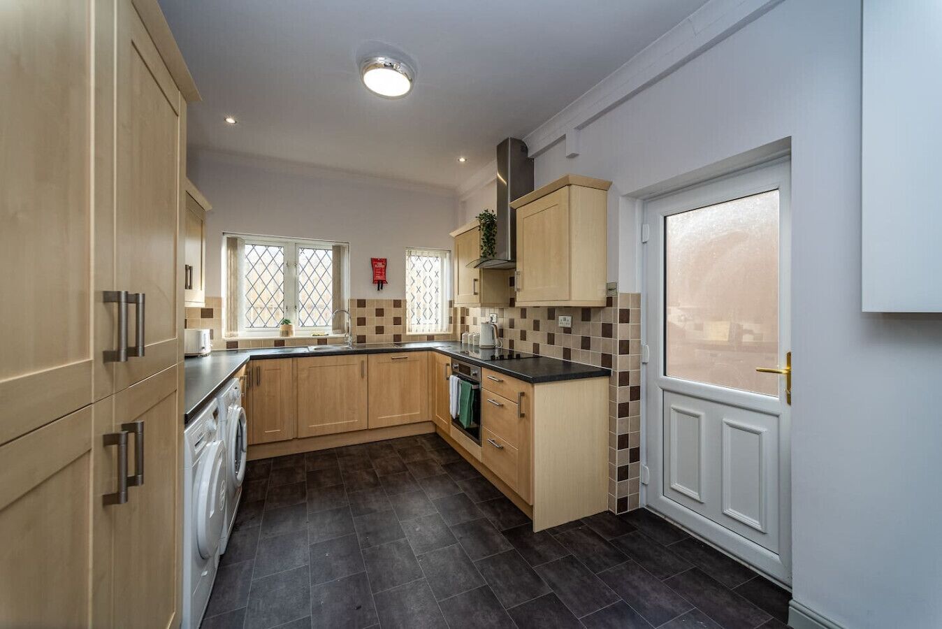 A kitchen with wooden cabinets, a black countertop, a white door, and a tiled backsplash.