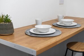Ein Holztisch mit weißen Tellern und Schüsseln, grauen Untersetzern und einem Blumentopf.