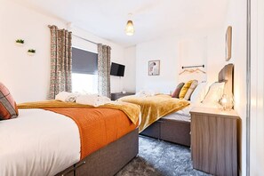 Een slaapkamer met twee bedden, een nachtkastje, een televisie en een raam met gordijnen.