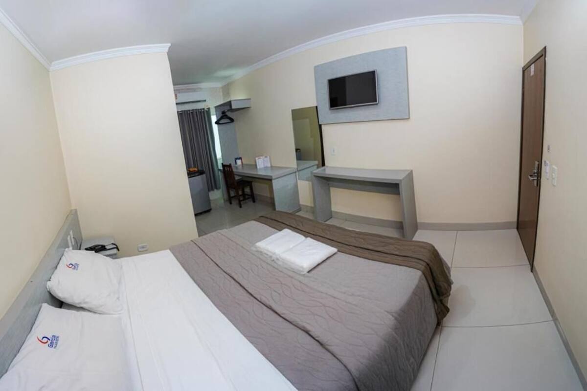 Habitación de hotel con cama, escritorio, televisor montado en la pared y baño al fondo.