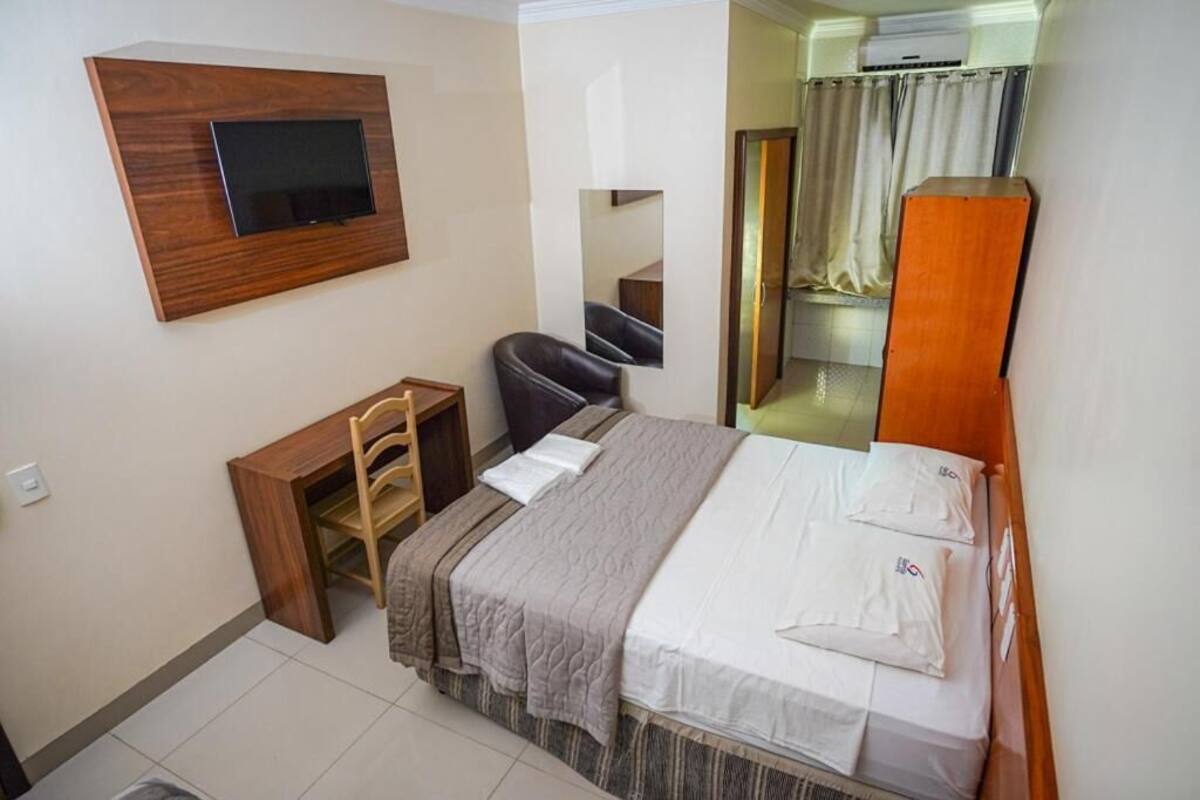 Habitación de hotel con cama, escritorio, silla, televisor montado en la pared y espejo.
