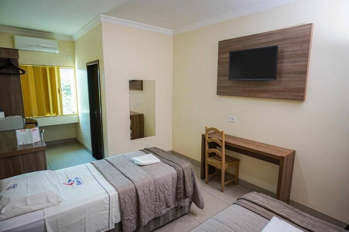 Habitación de hotel con dos camas, un escritorio, una silla, un televisor montado en la pared y un espejo.