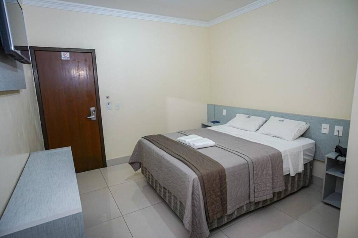 Una habitación de hotel con cama, escritorio, puerta y mesita de noche.