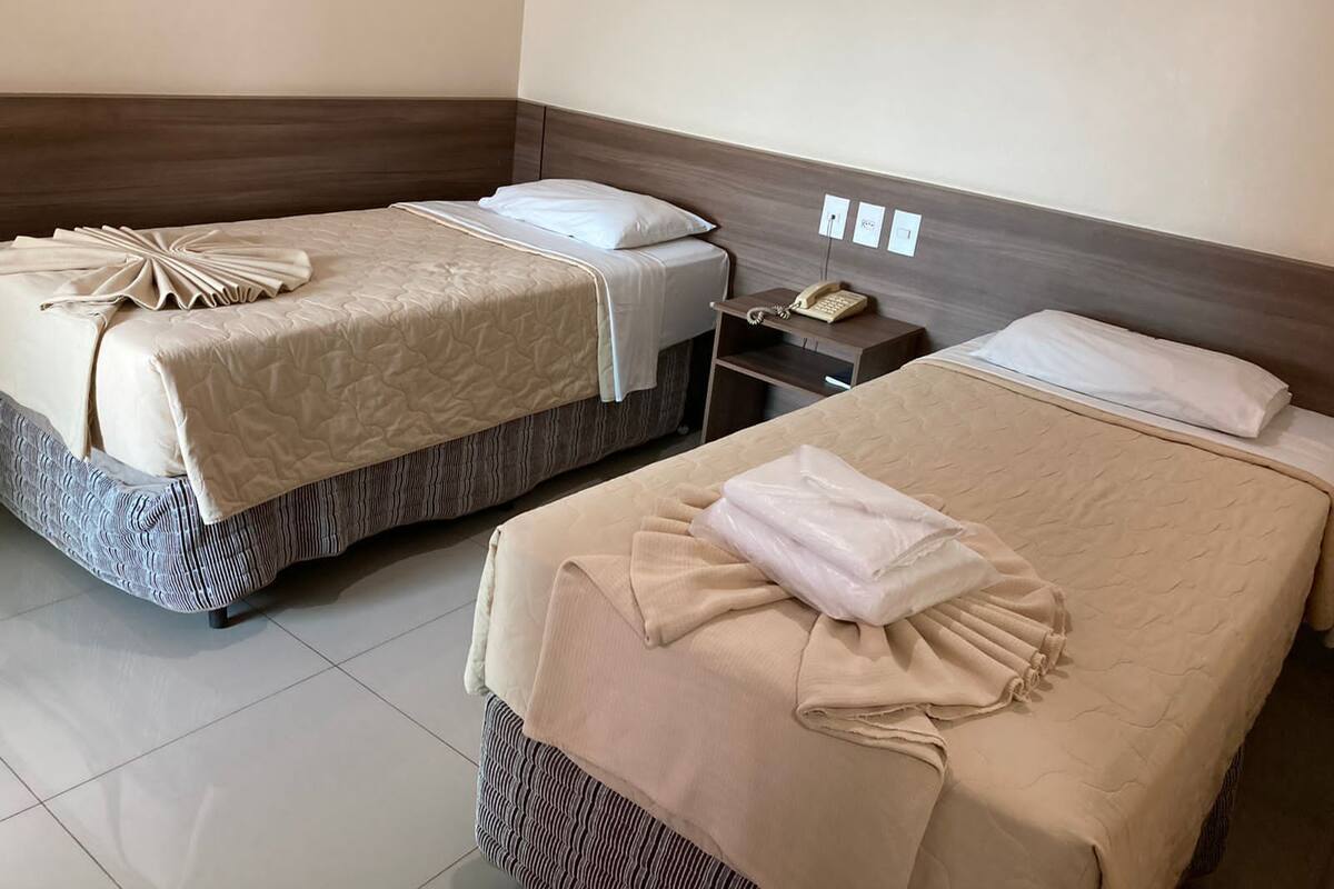 Dos camas con ropa de cama color beige, una mesita de noche con un teléfono y un interruptor de luz en la pared.