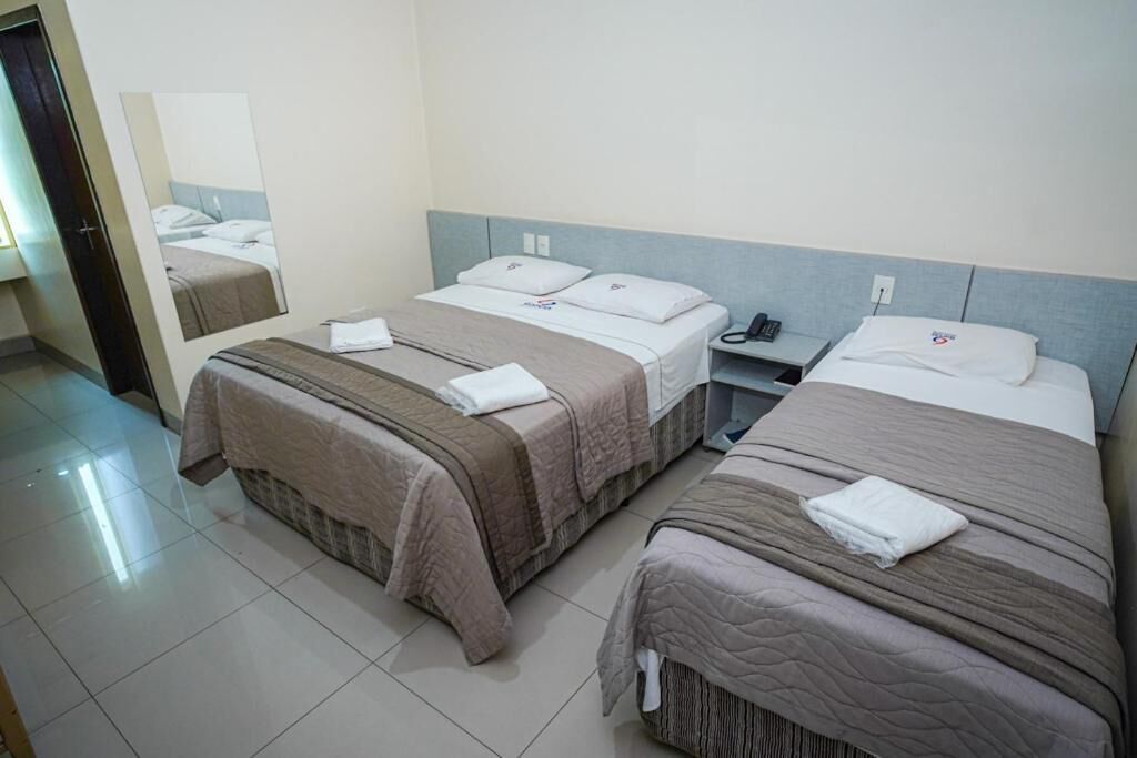 A hotel room with two beds, a bedside table, a mirror, and a door.