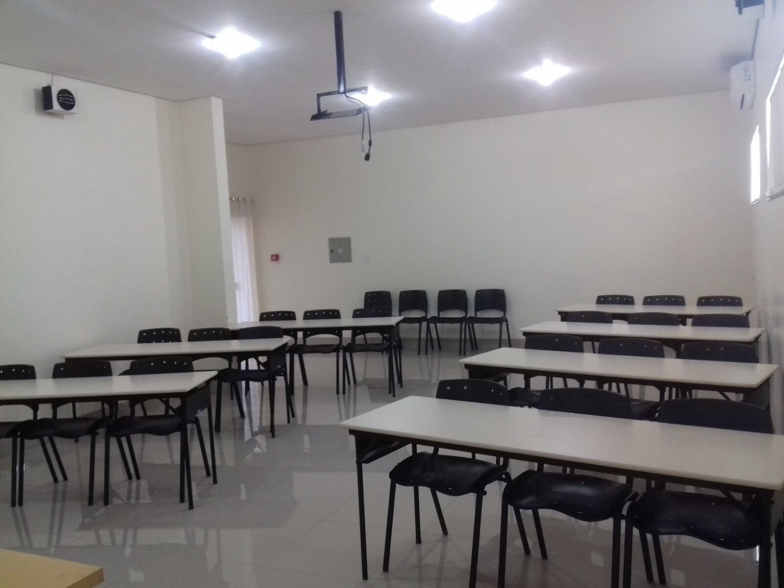 A classroom with rows of tables and chairs, a projector, and ceiling lights.