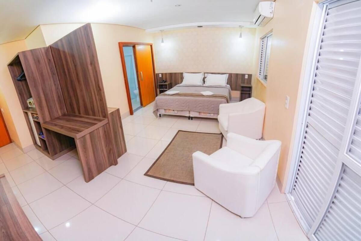 Un dormitorio con una cama, un sillón blanco, un armario de madera y un baño con inodoro y lavabo.