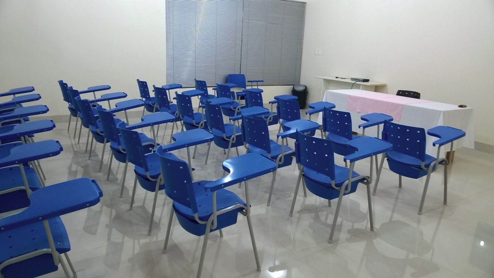 A classroom with rows of blue chairs and desks, a whiteboard, and a window with blinds.