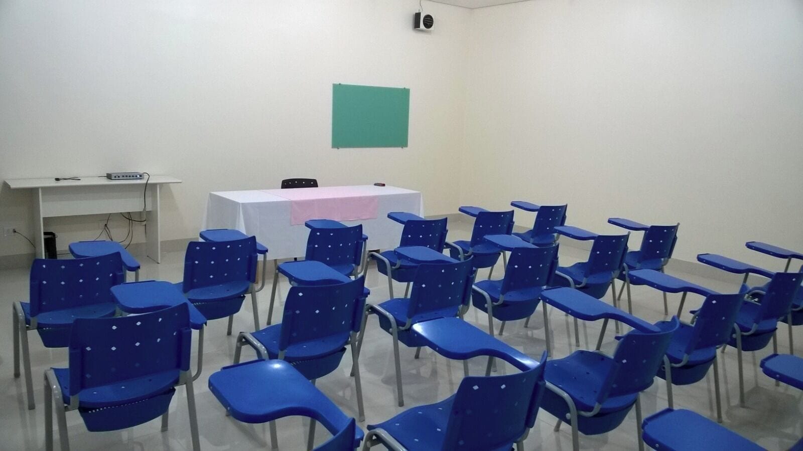 A classroom with rows of blue chairs and a white table with a pink cloth.