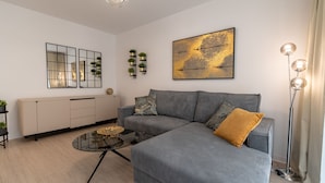 Ein modernes Wohnzimmer mit grauem Sofa, einem Glastisch, einer Stehlampe, einer Heizung und Wanddekoration.