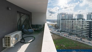 Ein Balkon mit Ventilator, einer Hängematte und Blick auf moderne Gebäude sowie eine Baustelle.