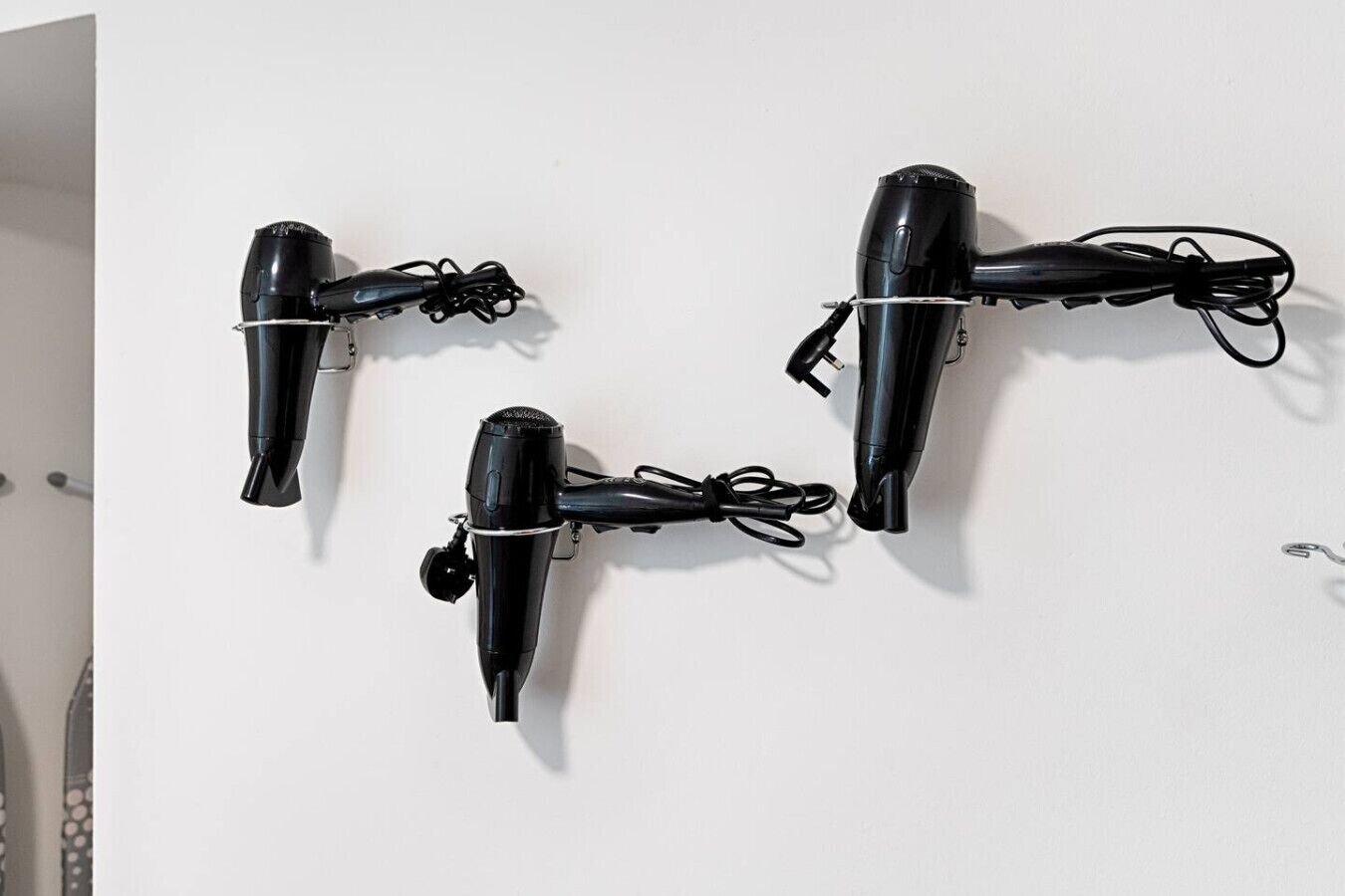 Three black hair dryers mounted on a white wall.