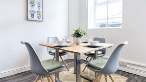A dining area with a wooden table, four grey chairs with green cushions, and a potted plant. - 2-Bed Apt • Kitchen • Parking • Ground Floor (Plasmarl)