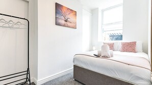 A hotel room with a bed, a painting on the wall, a window, and a clothing rack. - 2-Bed Apt • Kitchen • Parking • Ground Floor (Plasmarl)