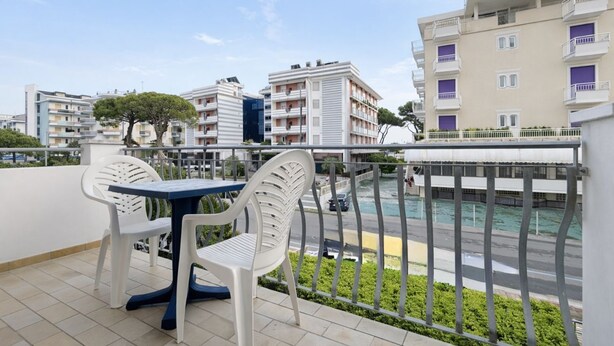 Un balcón con mesa y sillas, con vistas a una calle y una piscina.