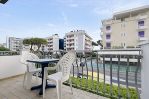 A balcony with a table and chairs, overlooking a road and a swimming pool. - Villa Luisa 4 - Carraro Immobiliare Jesolo (Lido di Jesolo)