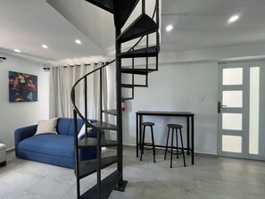 Uma sala de estar moderna com uma escada em espiral, um sofá azul, uma mesinha com dois banquinhos e uma porta com painéis de vidro jateado.