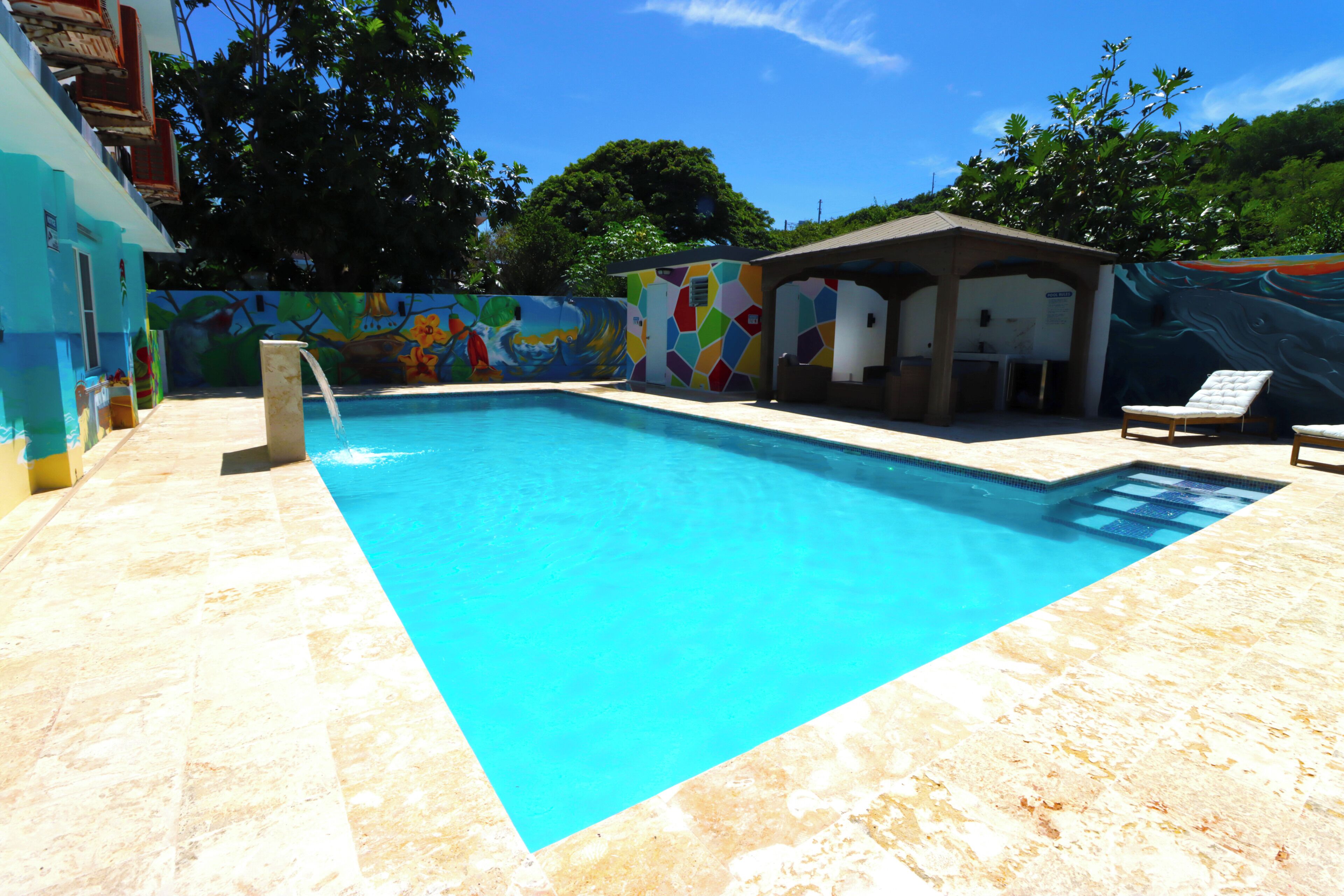 Une piscine avec une terrasse carrelée, un fauteuil de relaxation et une fresque colorée sur le mur.