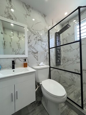 A bathroom with a marble wall, a white sink, a toilet, and a shower enclosure.