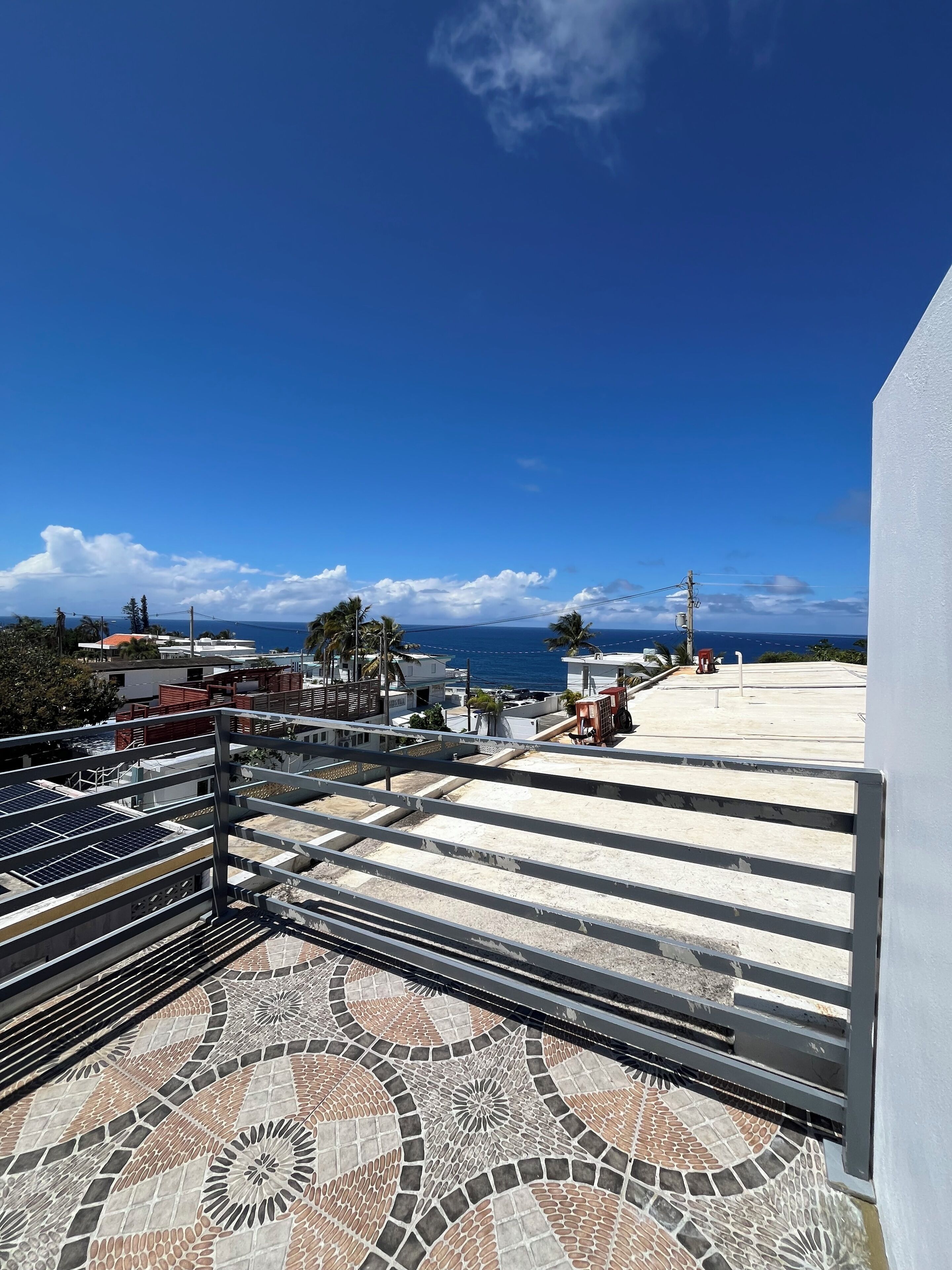 A rooftop terrace with a patterned floor, a metal railing, and a view of the ocean.