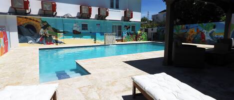 A swimming pool area with lounge chairs and a mural on the building.