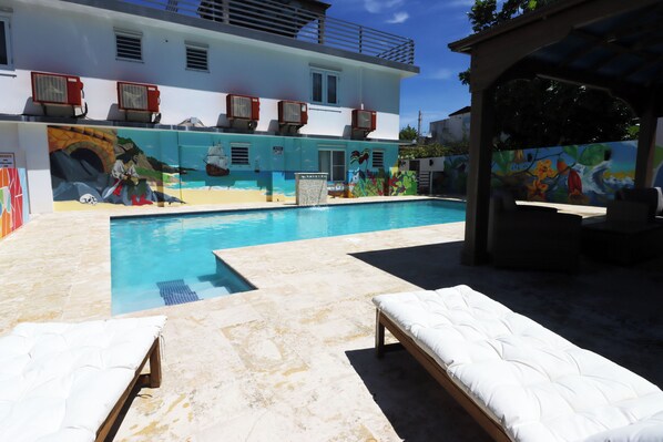 Uma área de piscina com espreguiçadeiras e um mural no edifício.