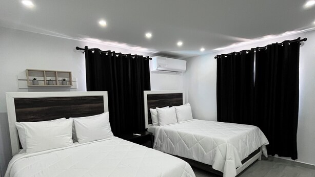 Habitació d'hotel amb dos llits, una taula de nit, una estant amb objectes decoratius i un aparell d'aire condicionat.