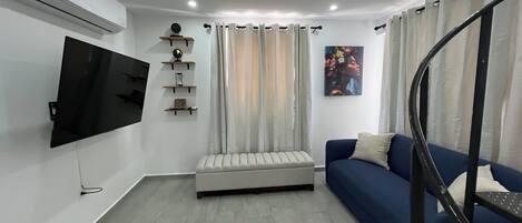 Una sala de estar moderna con un televisor de pantalla plana, un sofá, un banco y una escalera.