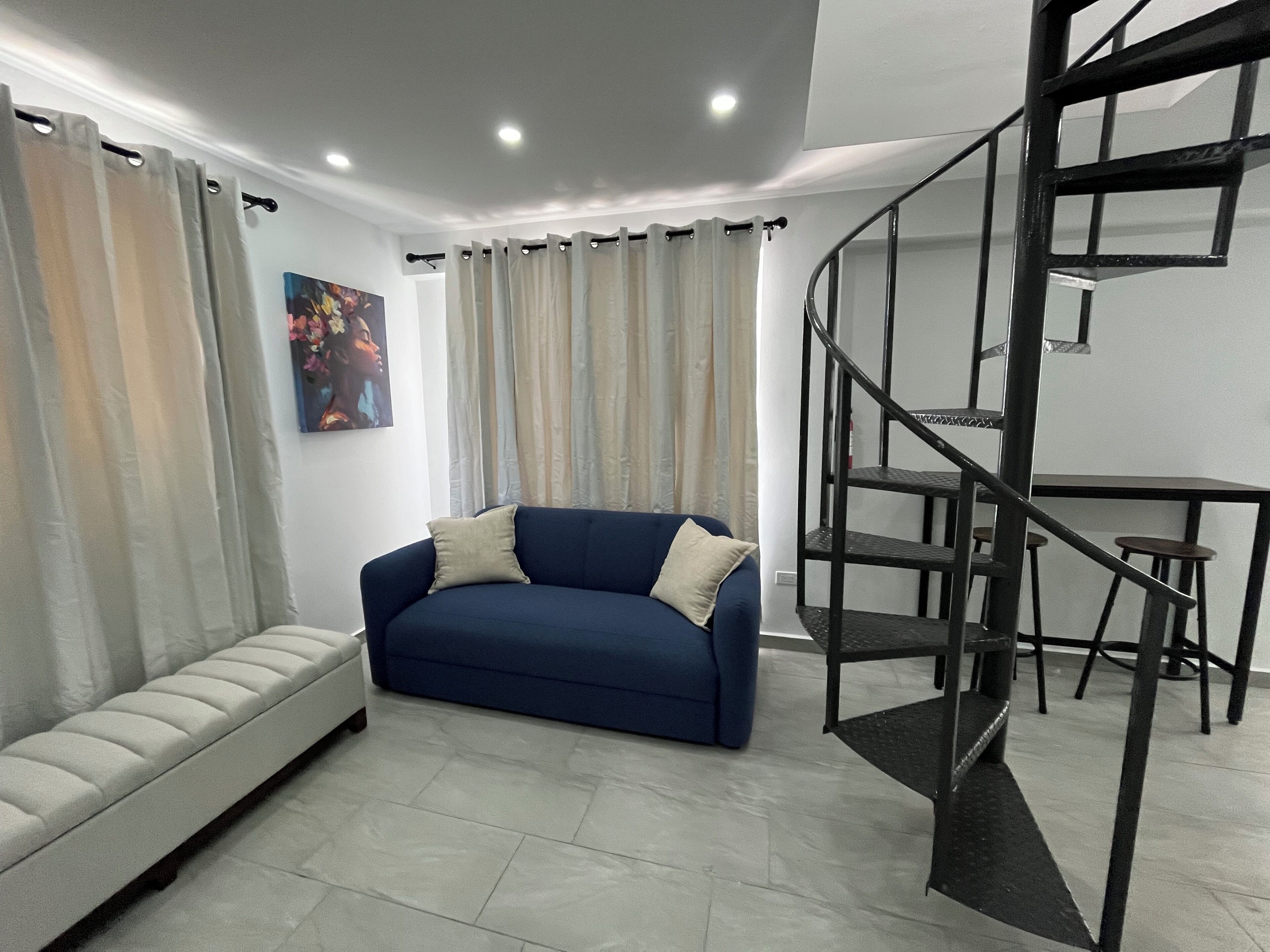 A living room with a sofa, a painting, a staircase, and a dining area.