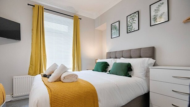 A hotel room with a bed, a dresser, a radiator, and a window with curtains. - Spacious Home • Parking • Kitchen • Ideal for Work (Port Tennant)