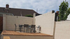 A wooden deck with a table and chairs, surrounded by a white wall. - Spacious Home • Parking • Kitchen • Ideal for Work (Port Tennant)
