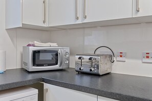 Una cocina con gabinetes blancos, un microondas y un tostador sobre una encimera gris.