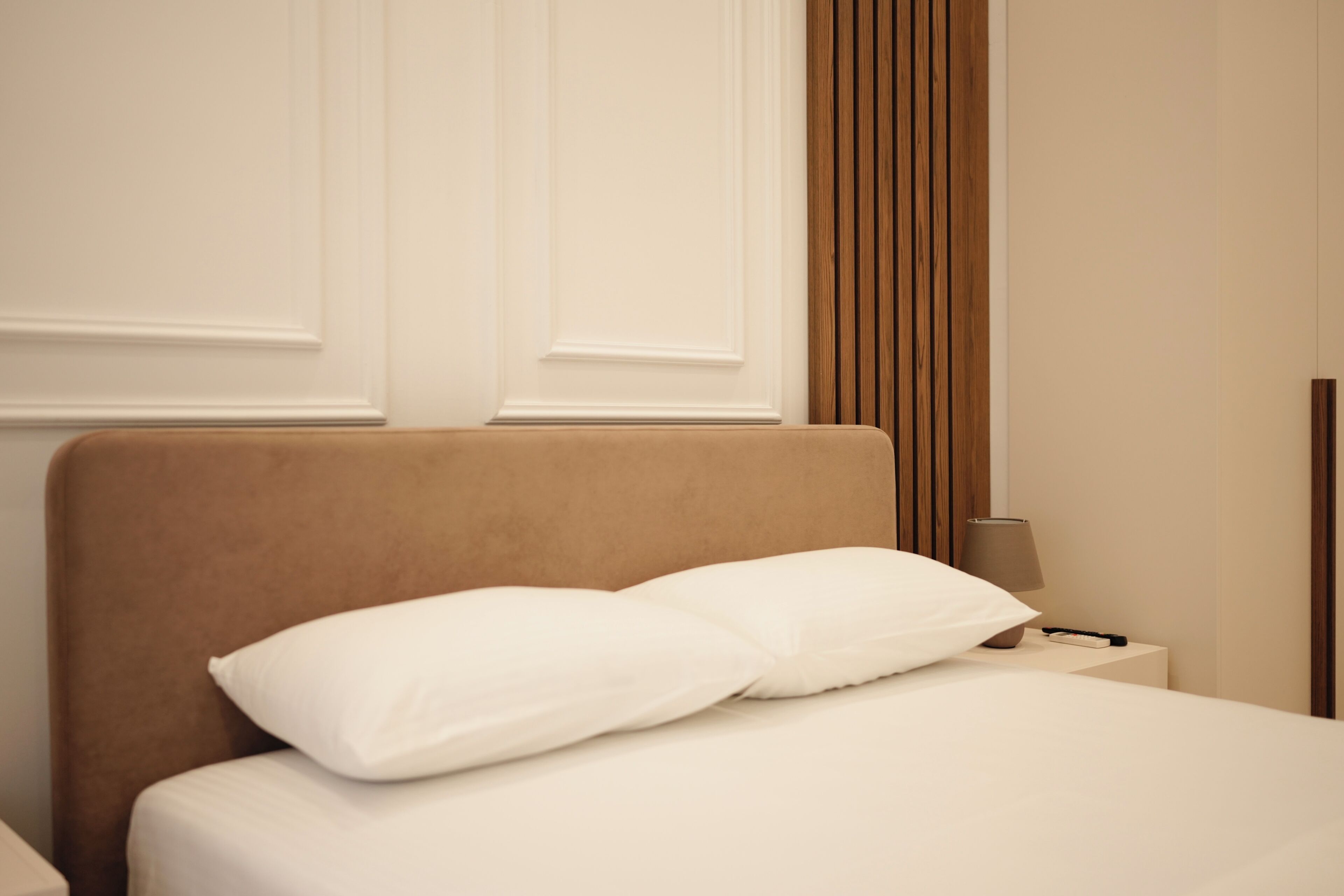 A neatly made bed with white bedding and a brown headboard in a hotel room.