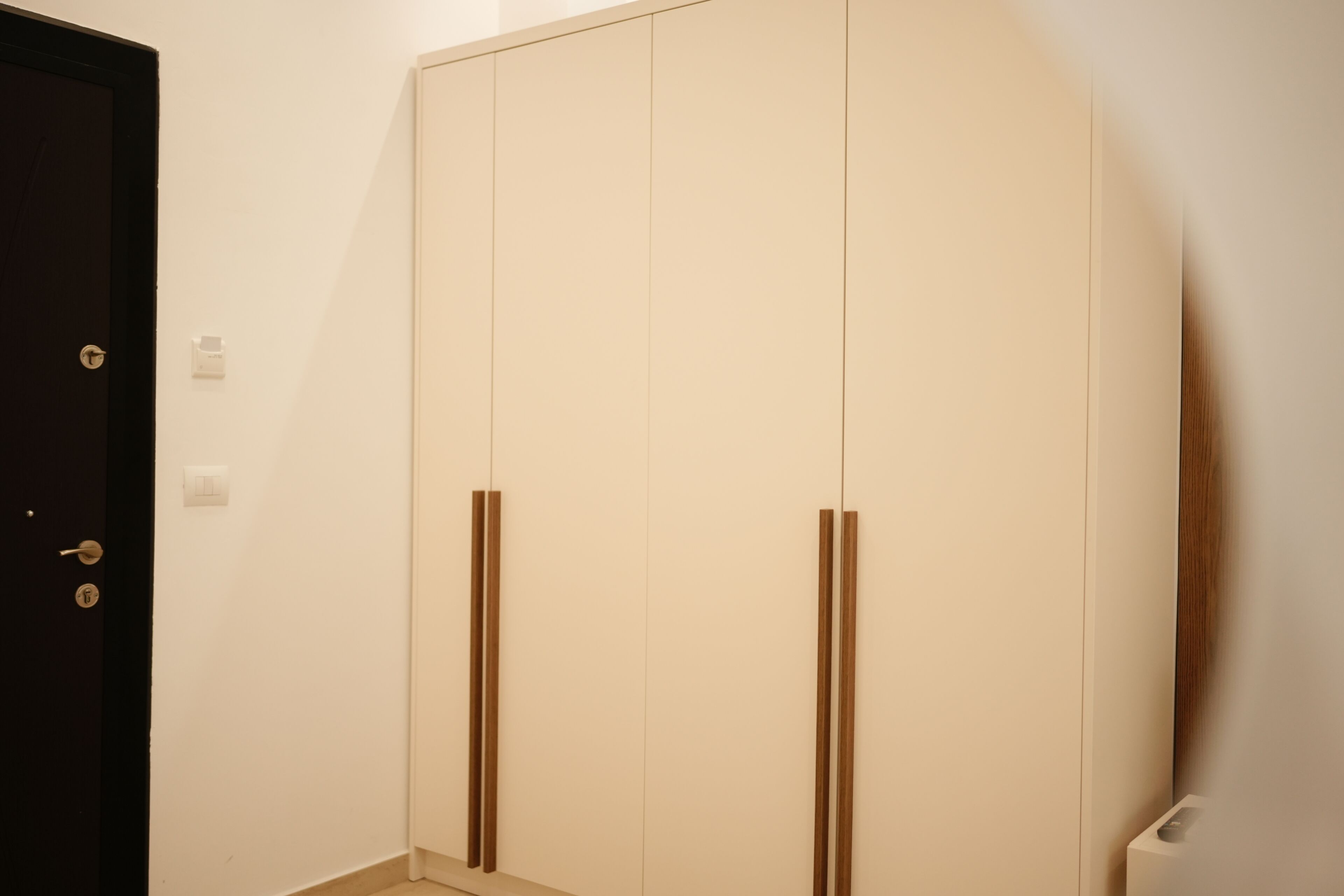 Ein Zimmer mit einer dunklen Tür, einem weißen Kleiderschrank mit vertikalen Griffen und einem weißen Heizkörper.