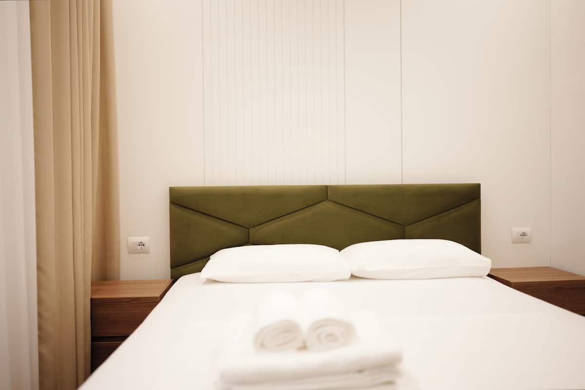 A neatly made bed with a green headboard, white pillows, and a wooden nightstand with a power outlet.