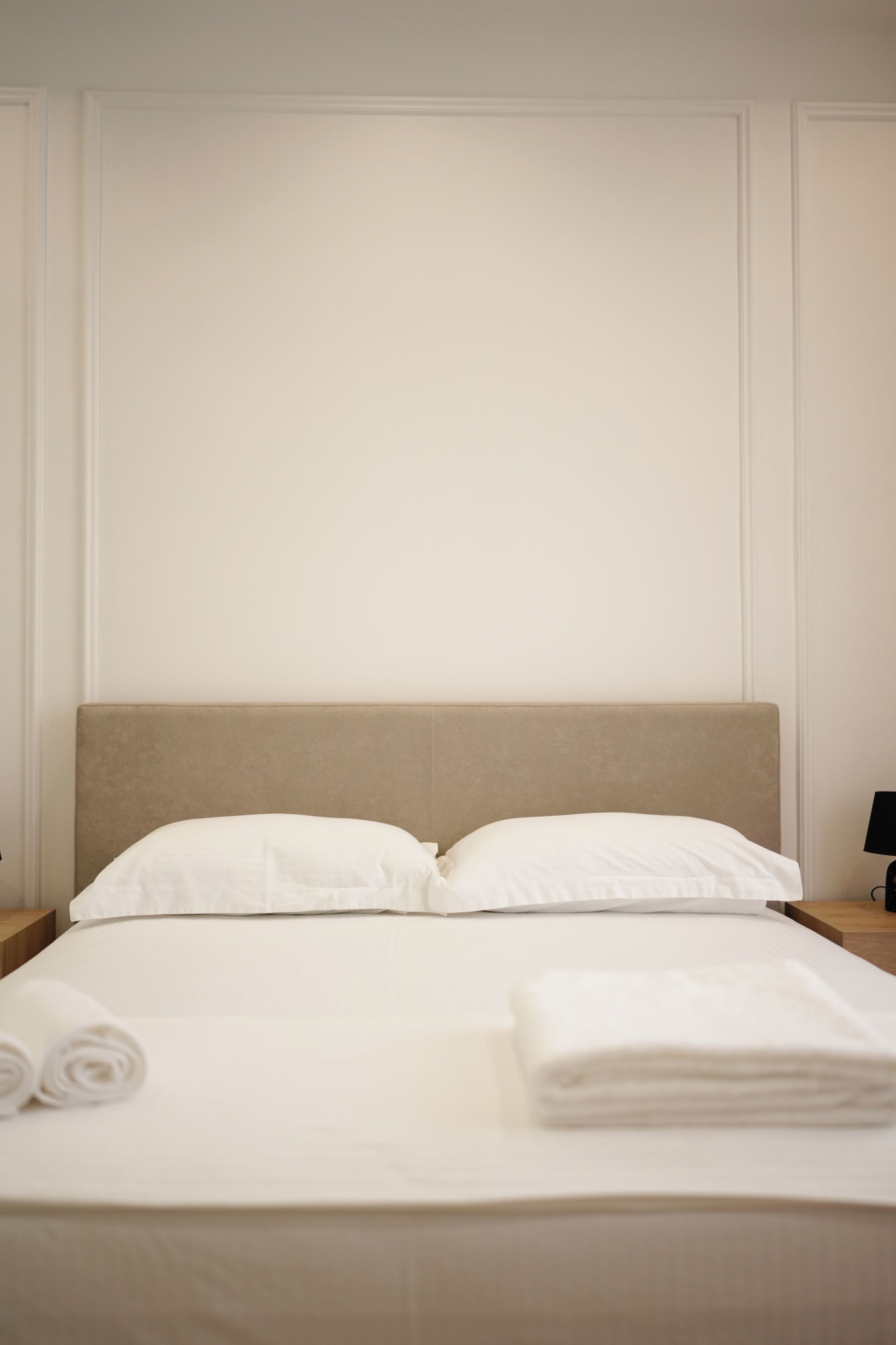 A neatly made bed with white linens, a headboard, and two bedside tables with lamps.