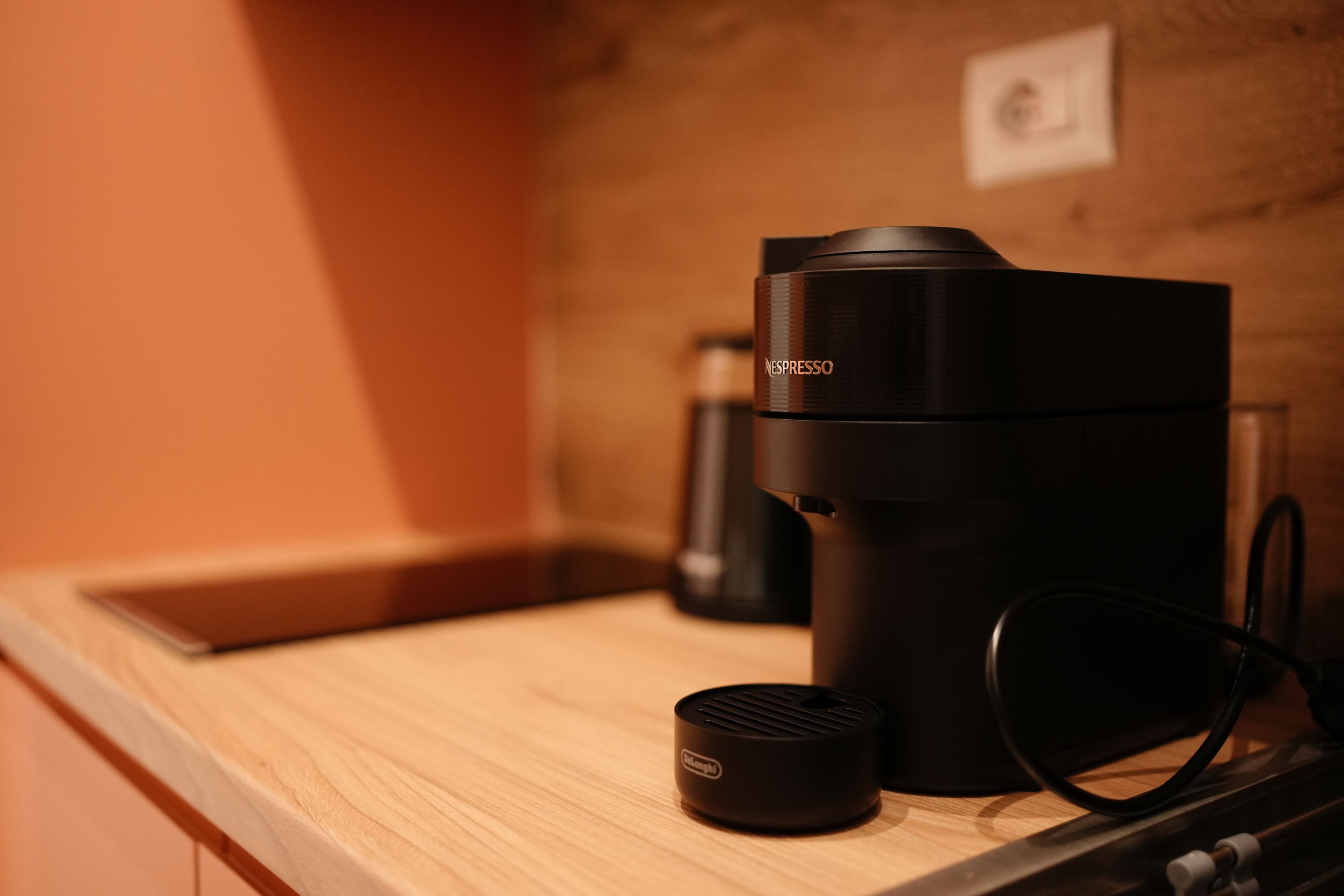 A coffee machine on a wooden countertop with a wall-mounted outlet in the background.