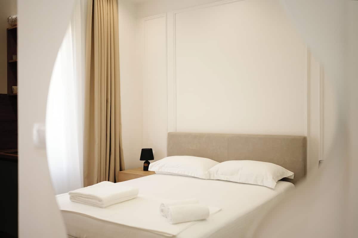 A hotel room with a bed, a nightstand, a lamp, and a window with curtains.