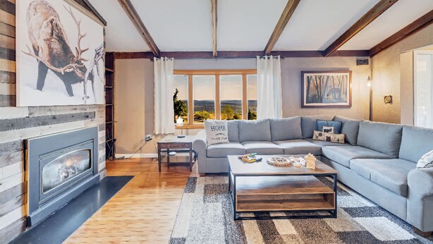A living room with a fireplace, a sofa, a coffee table, and a large window with a view. - Mountain Views Private Pond Mins 2 Elk Mountain (Union Dale)