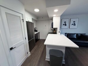 Eine moderne Küche mit weißen Schränken, einem Edelstahlkühlschrank, einer weißen Arbeitsplatte und einem schwarzen Mülleimer.