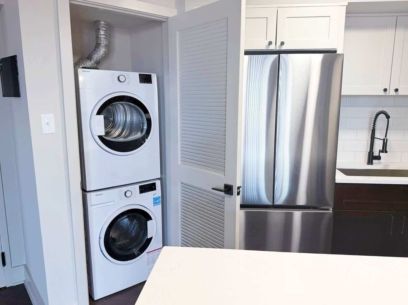 Une cuisine compacte équipée d’un réfrigérateur en acier inoxydable, d’un four à deux portes et d’un lave-linge.