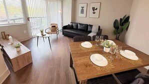 En moderne stue med spiseplads, en sort lædersofa og et spisebord dækket til fire personer.