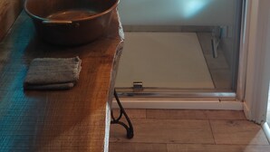 Une douche avec une porte en verre, un banc en bois et un lavabo en métal.