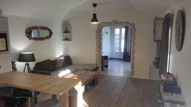 Un salon chaleureux avec un canapé, une table en bois, une lampe et une arche en pierre qui mène à un balcon.